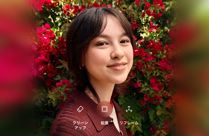 茶髪の人物が微笑んでいる写真。茶色のセーターを着て、赤い花に囲まれている。写真上に表示されている「クリーンアップ」、「拡張」、「リフレーム」のオプションを使って、AIによる写真編集を行ったもの