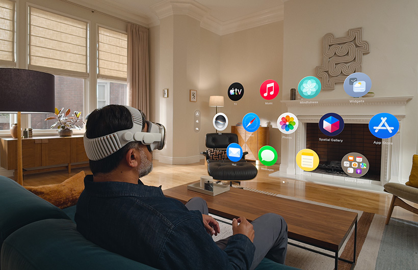 一名使用者戴著 Apple Vision Pro 坐在客廳的沙發上，正在啟動主畫面