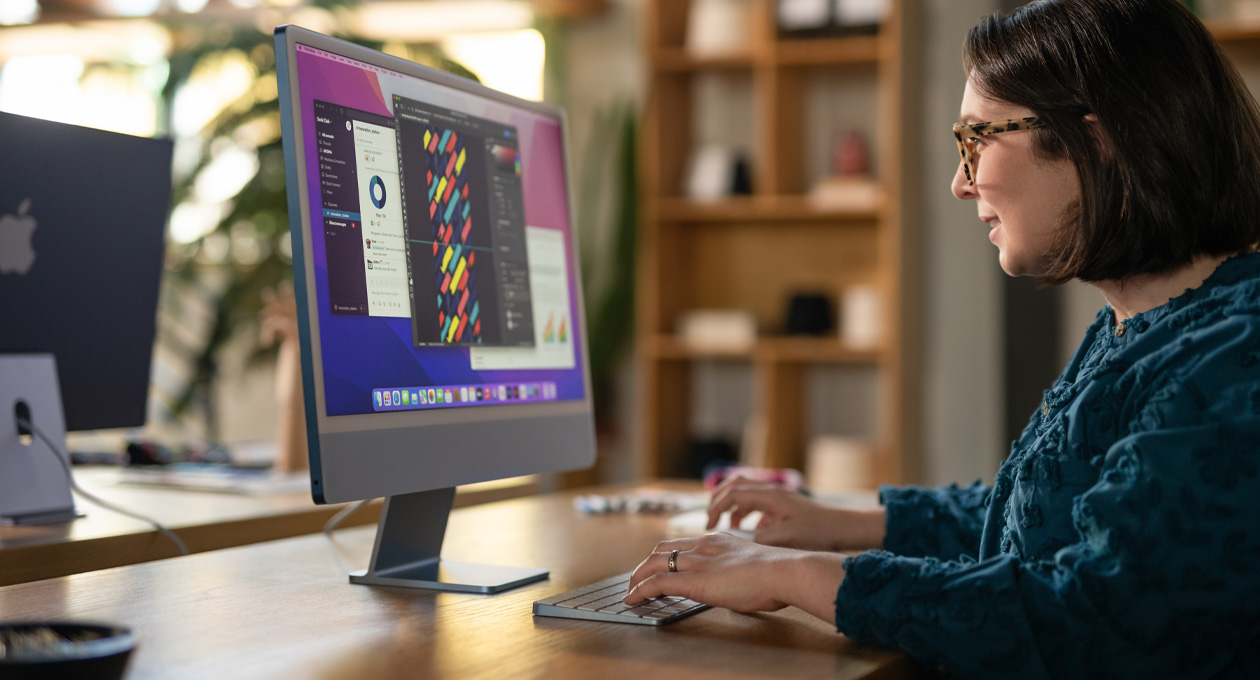 Seseorang bekerja di iMac yang menampilkan aplikasi desain yang penuh warna di sebuah kantor