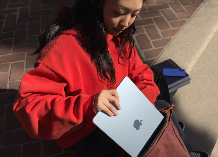 En person sidder på en trappe, i gang med at lægge en MacBook i sin rygsæk.