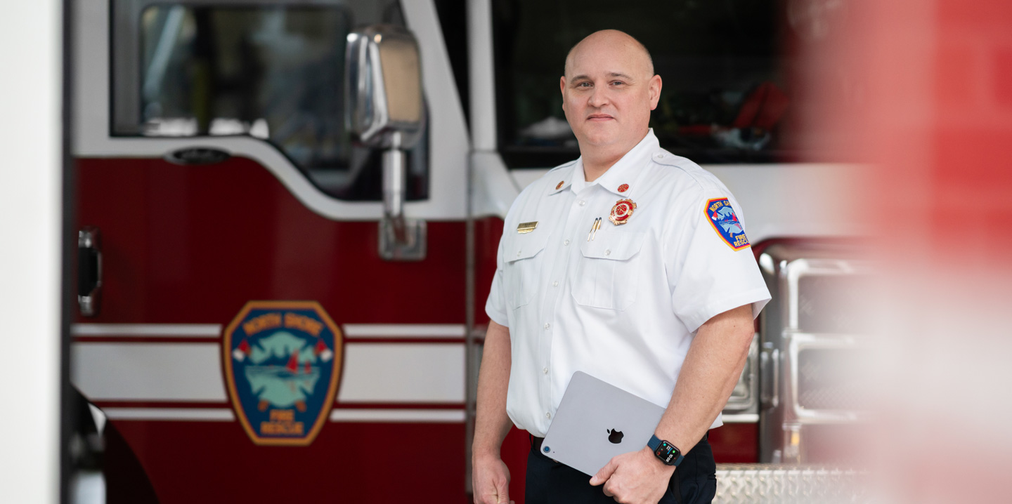 Der Feuerwehrchef steht vor einem Feuerwehrauto, hält ein iPad und trägt eine Apple Watch
