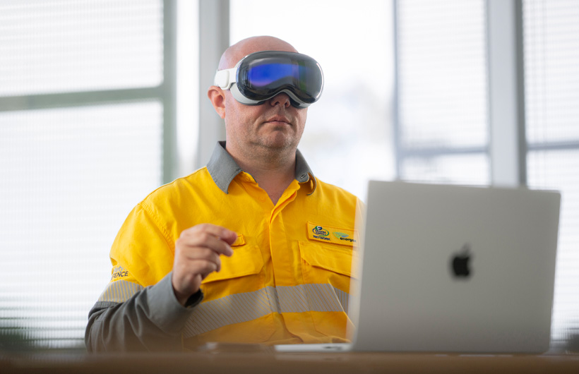 Ein Mitarbeiter arbeitet mit einer Apple Vision Pro, während ein MacBook Pro in Silber offen auf dem Schreibtisch steht