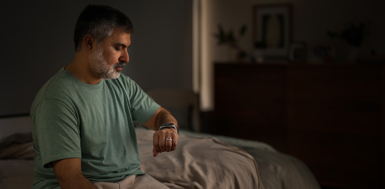 Un homme assis sur son lit consulte son Apple Watch.