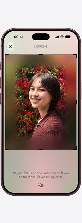 iPhone 18 Pro, vỏ ngoài mặt trước, tính năng Định Lại Khung Không Gian đang được sử dụng để định lại khung cho ảnh chụp cận cảnh một người phụ nữ với những bông hoa hồng đỏ ở phía sau